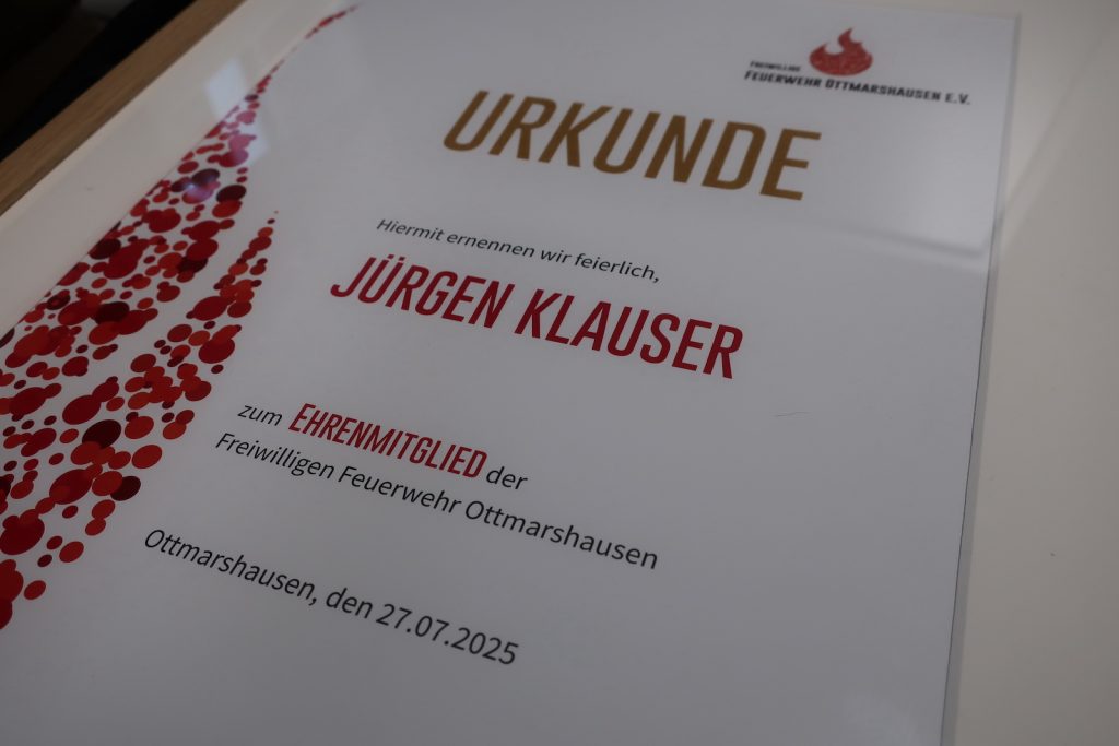 Nahaufnahme einer Urkunde, die Überschrift ist golden, Hervorhebungen sind in kräftigem Rot gehalten. Der Text lautet "Hiermit ernennen wir feierlich Jürgen Klauser zum Ehrenmitglied der Freiwilligen Feuerwehr Ottmarshausen".