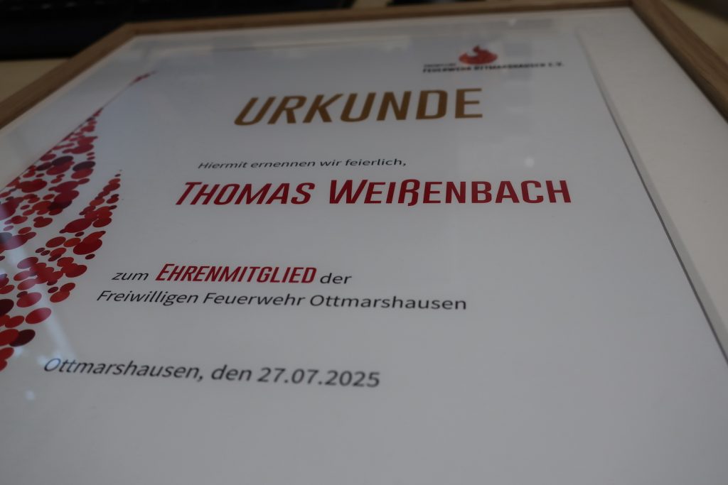 Nahaufnahme einer Urkunde, die Überschrift ist golden, Hervorhebungen sind in kräftigem Rot gehalten. Der Text lautet "Hiermit ernennen wir feierlich Thoms Weißenbach zum Ehrenmitglied der Freiwilligen Feuerwehr Ottmarshausen".